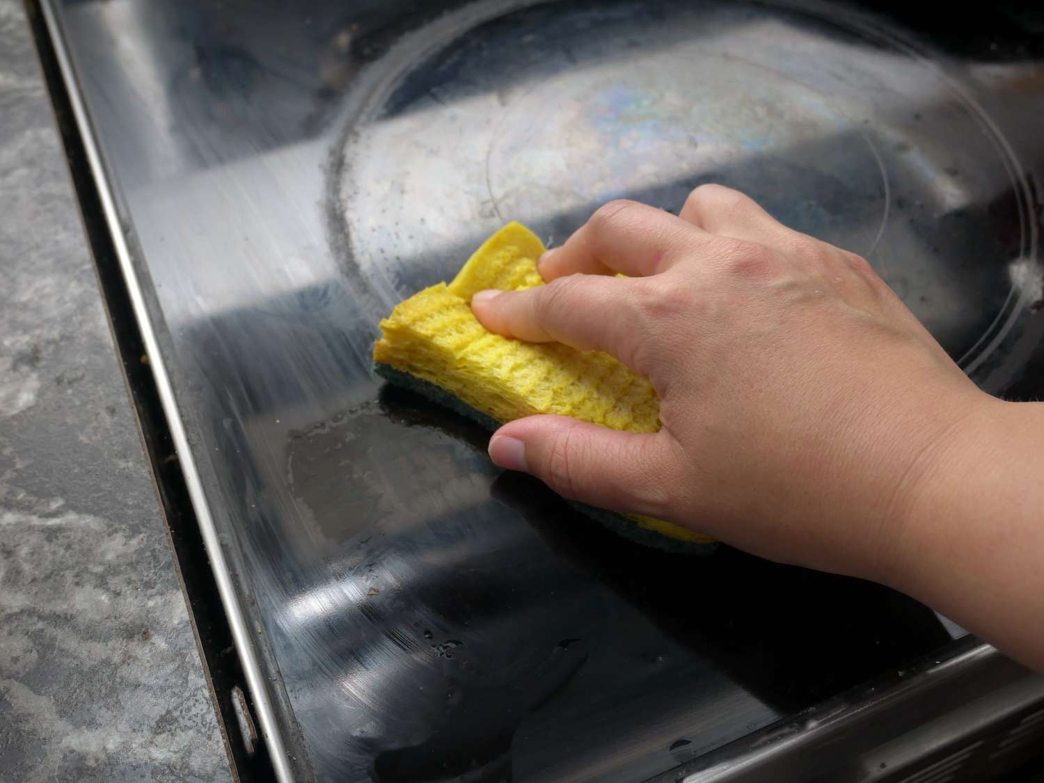 hand cleaning glass top stove with sponge