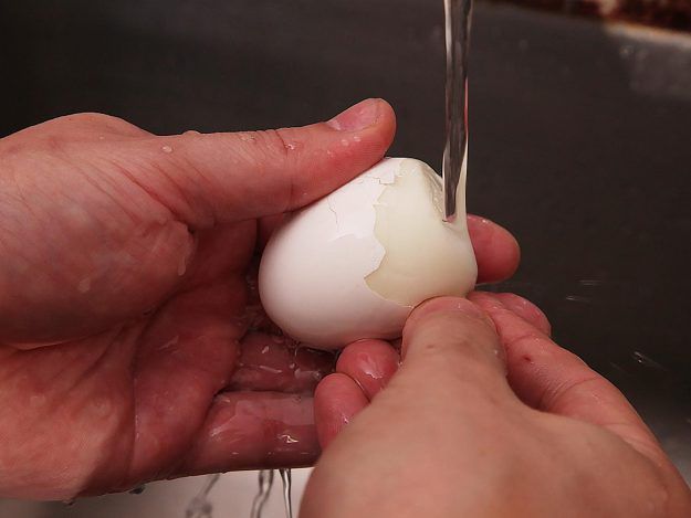 Boiled egg being peeled under running water.