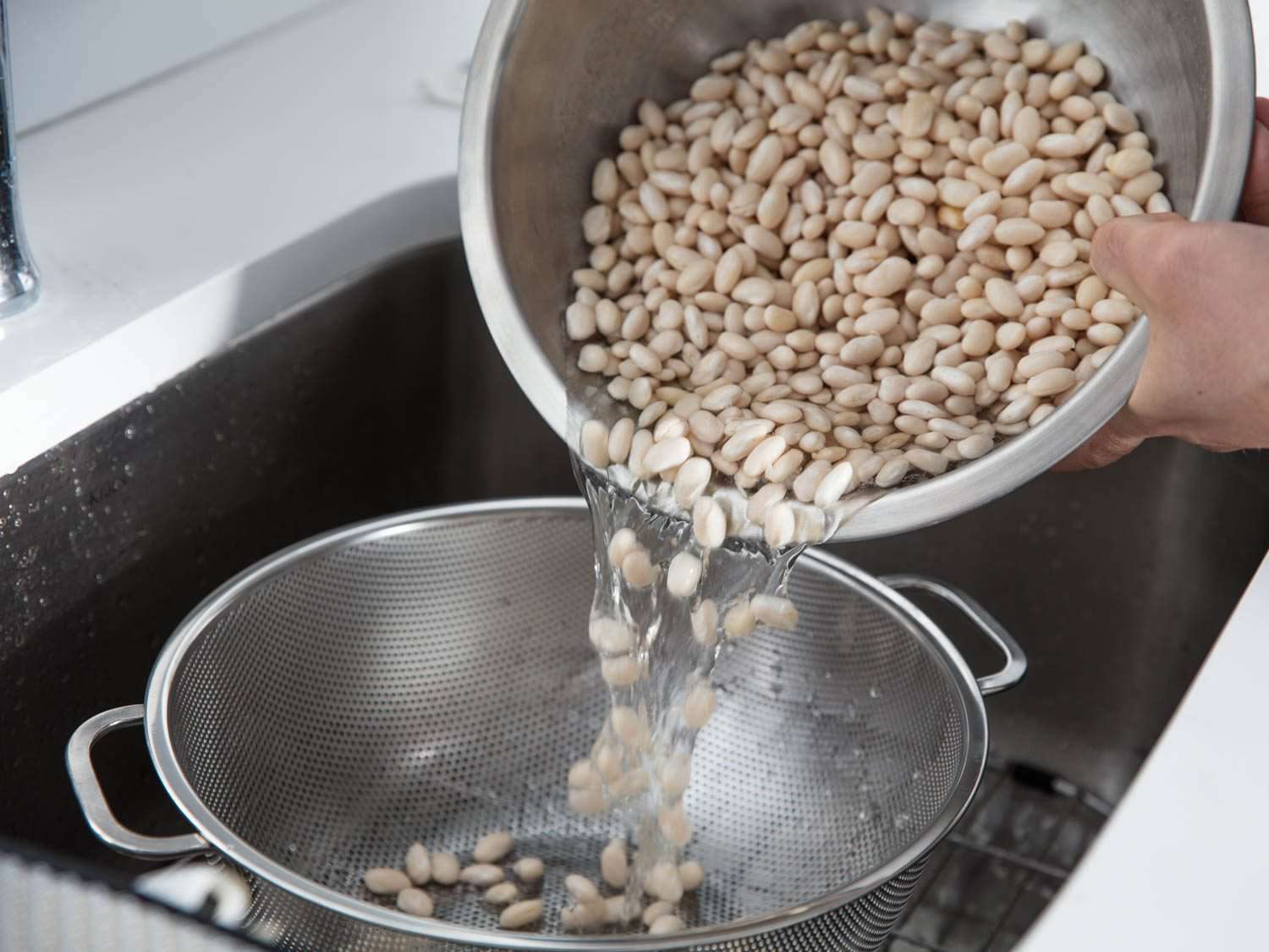 把一大碗泡好的白豆倒进水槽里的滤锅里
