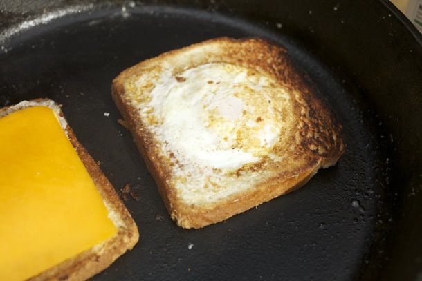 在煎锅里煎的两片面包，一片中间有一个煎蛋，另一片上面有一片奶酪