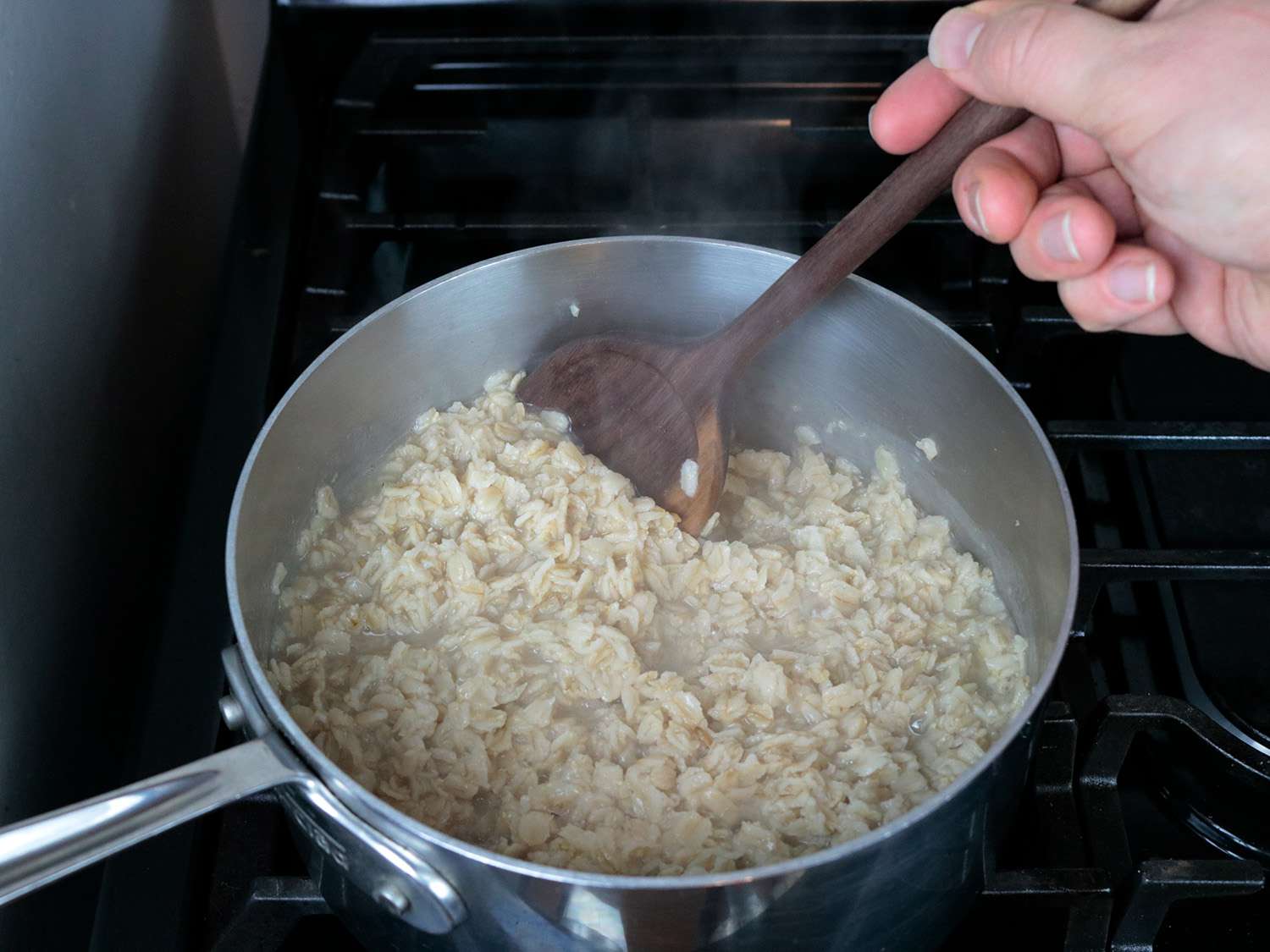a thin handled wooden spoon stirs oatmeal in a pot