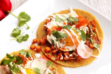 Two tacos made of sweet potatoes, sage, and fried eggs on corn tortillas.