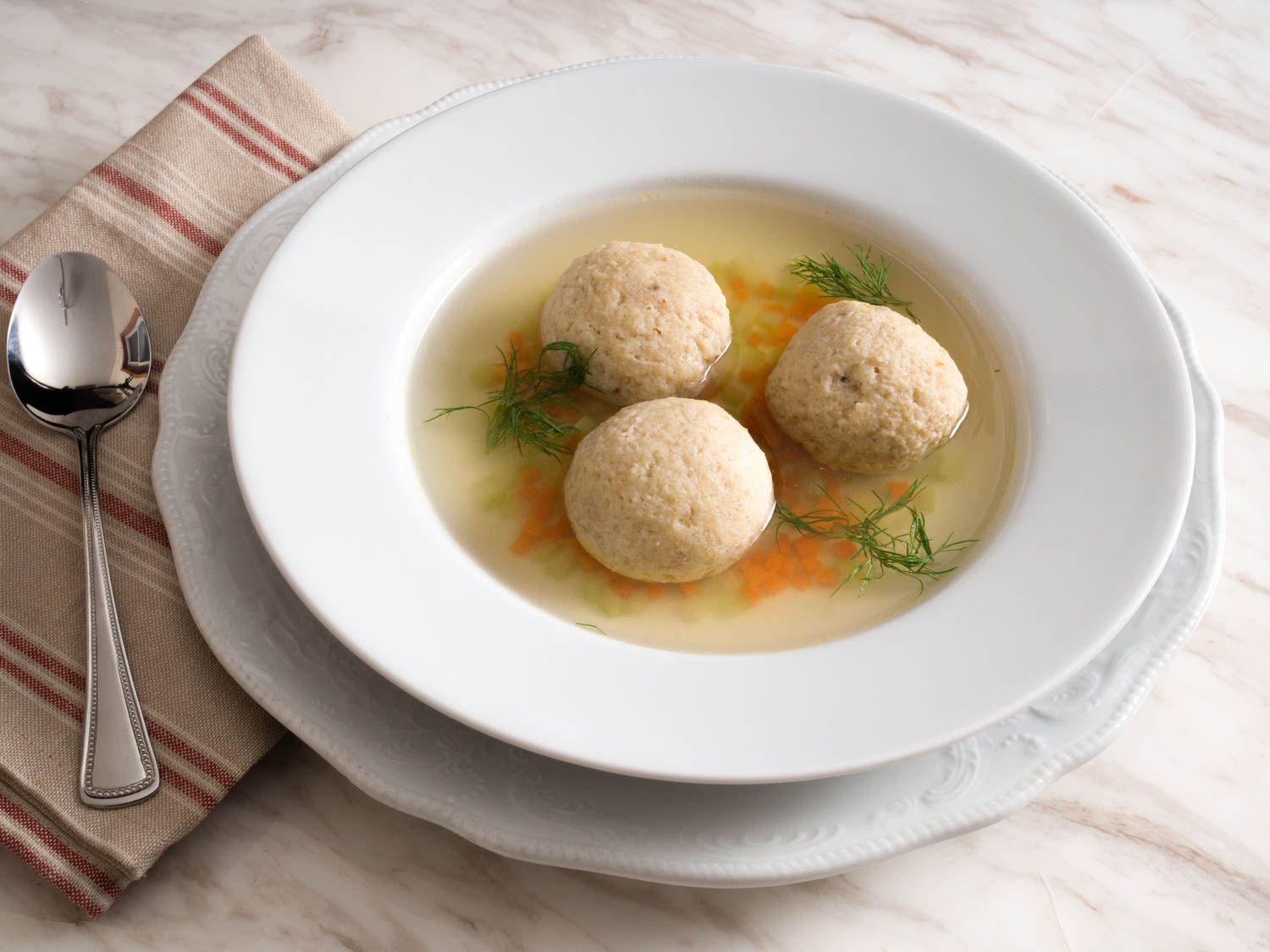 A close-up of a white bowl filled with matzo ball soup.