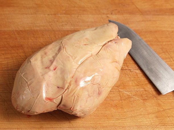 砧板上放着一把厨刀，旁边放着一整只鹅肝。
