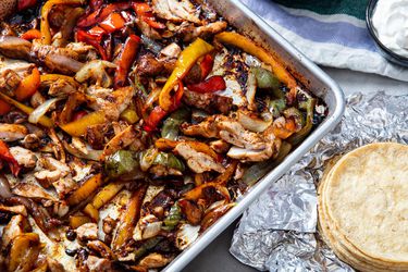 Sheet Pan chicken fajitas with a stack of tortillas nearby.