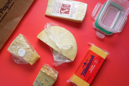 a variety of cheese on a red backdrop with parchment paper and a food container