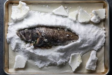 整个烤黑鲈鱼,葬在密苏里州und of salt on a baking sheet is exposed after the salt crust was cracked and removed.