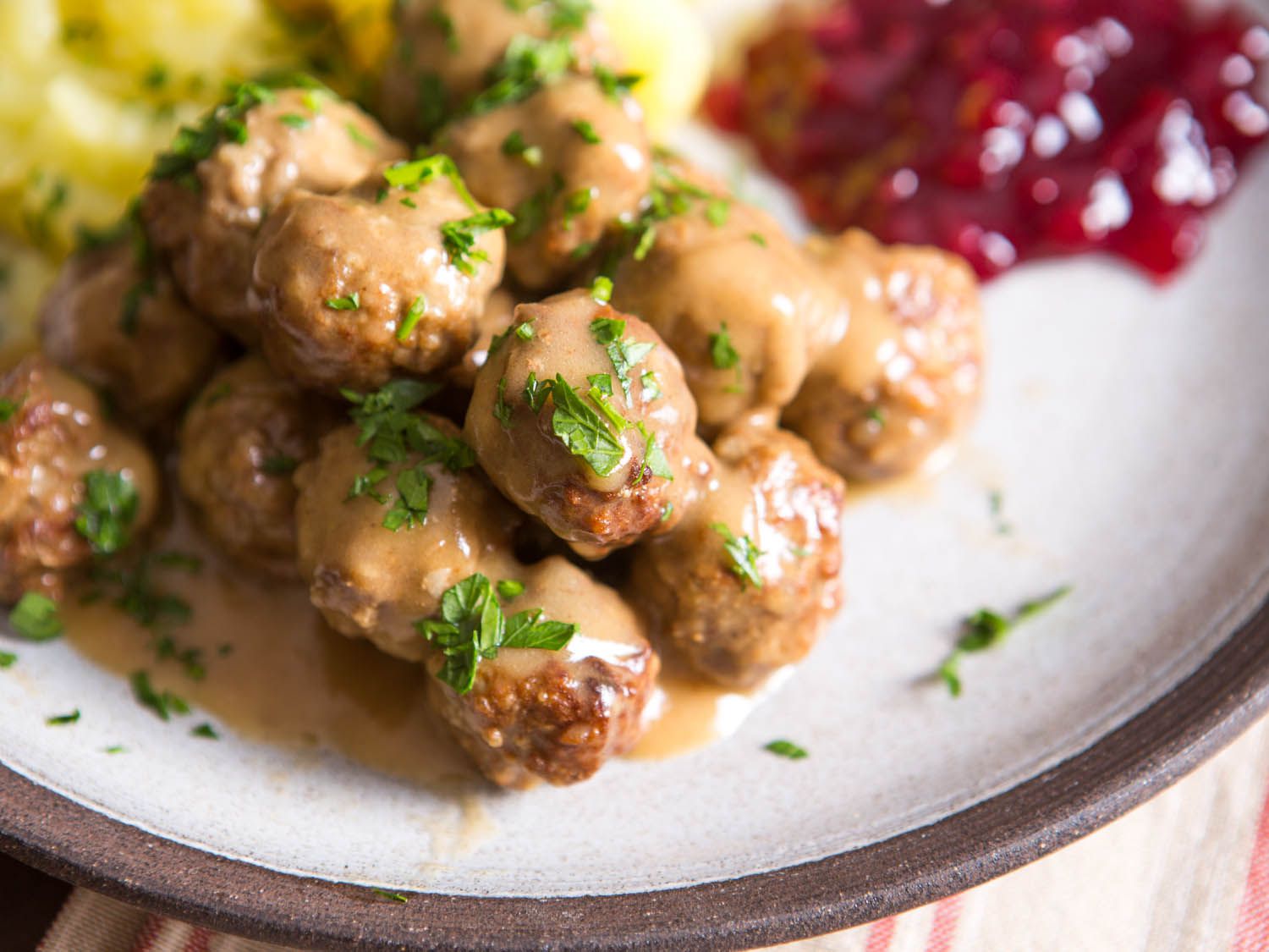 A plate of Swedish meatballs coated in a rich gravy served with lingonberry sauce and potatoes
