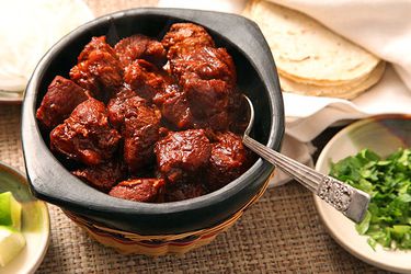 A small bowl of carne adovada with cilantro and tortillas next to it.