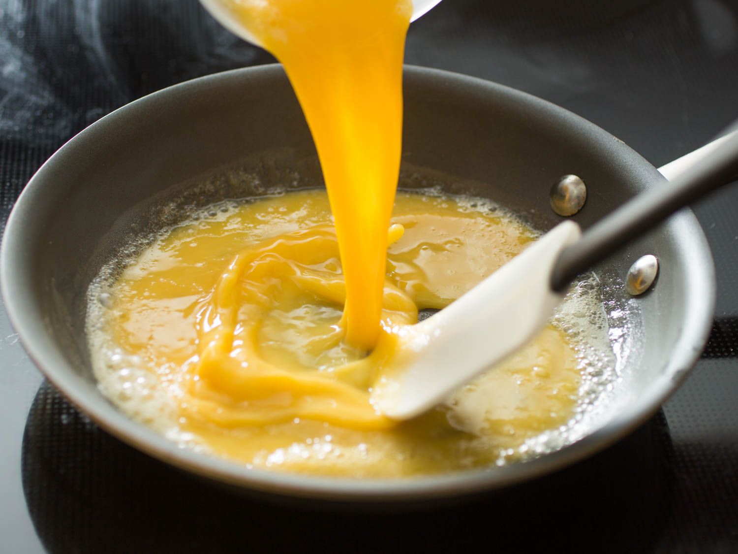 Pouring egg into a skillet for scrambled eggs and stirring with a flexible spatula