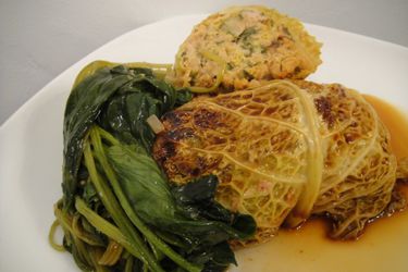 Asian Cabbage Rolls with Spicy Pork on a plate with sauce and greens.