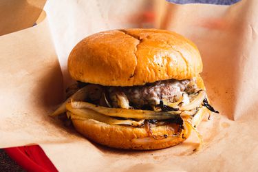 An Oklahoma style onion burger on deli paper in a red plastic deli basket.