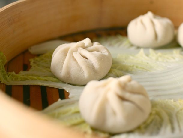 Xiao long bao dumplings arranged on napa cabbage leaves in a bamboo steamer, ready to be cooked.