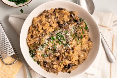 Finished and garnished mushroom risotto in a bowl with cheese and herbs on the periphery.