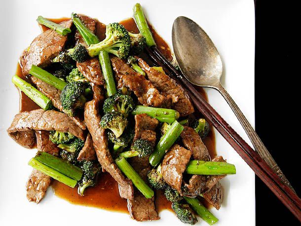 Overhead view of stir-fried beef with broccoli and oyster sauce on a platter with a serving spoon and chopsticks.