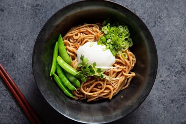 A bowl of mazemen ramen topped with an egg, snap peas, and sprouts