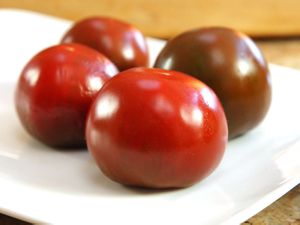 Whole ripe tomatoes on a plate with their top sides down.