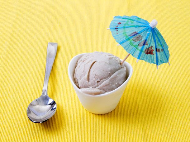 一小杯白色的素食香蕉椰子冰淇淋，里面插着一把蓝色的纸伞，旁边放着一把勺子