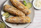 elotes (grilled Mexican street corn) on a plate with limes and chili powder