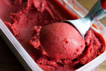 Closeup of plum sorbet being scooped from a container.