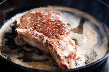 A bone in steak cooking in a cast iron skillet.