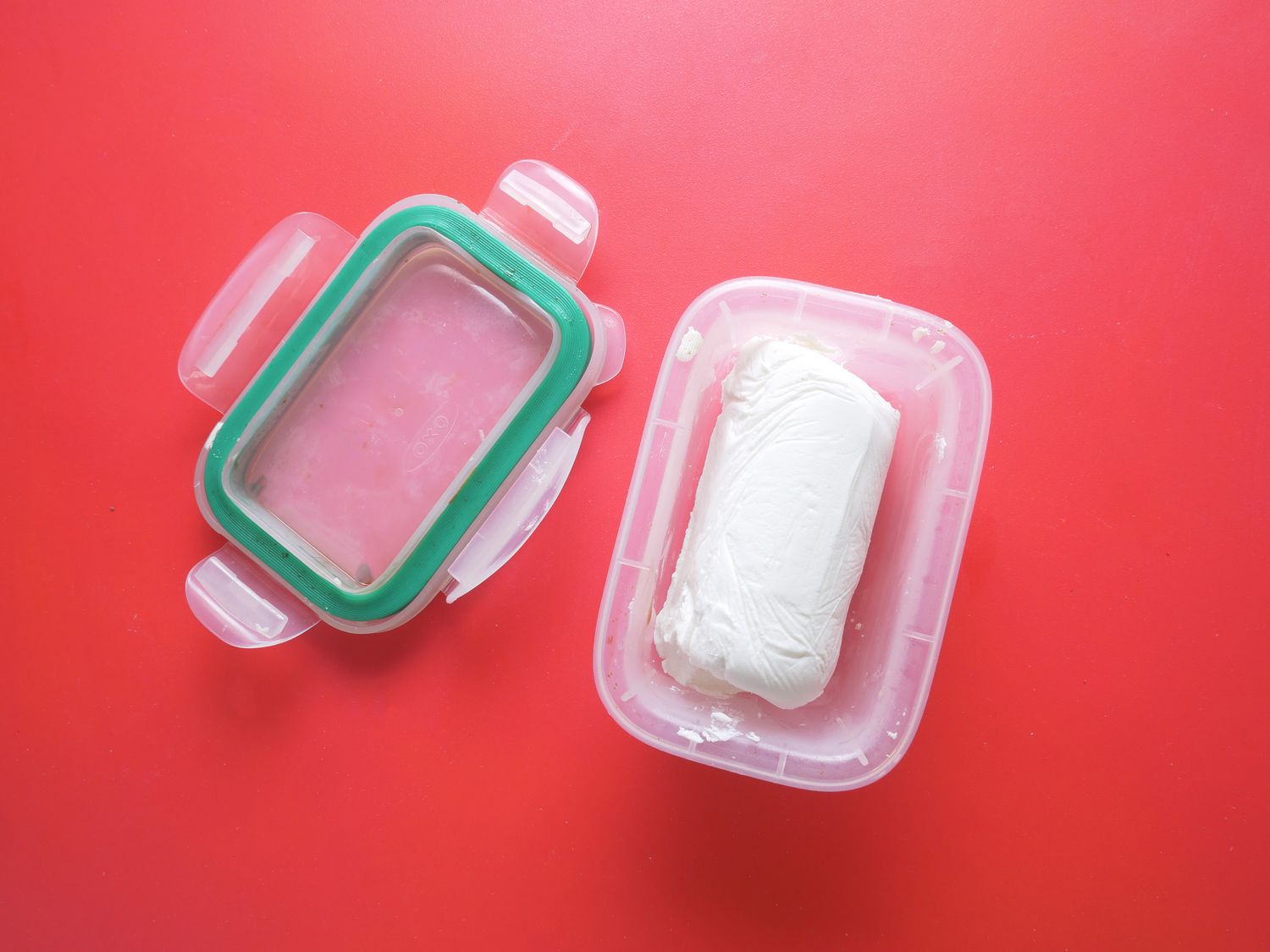 a piece of goat cheese in a small food storage container on a red surface.