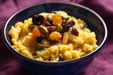 Bowl of semolina halva topped with spiced nuts and dried fruit