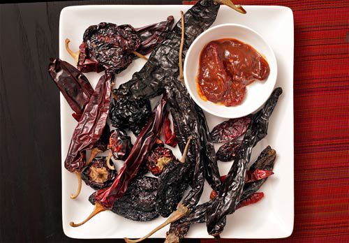 Square white plate covered in dried whole chiles with a small bowl of chile paste
