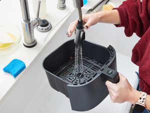 A person cleaning an air fryer basket in the sink