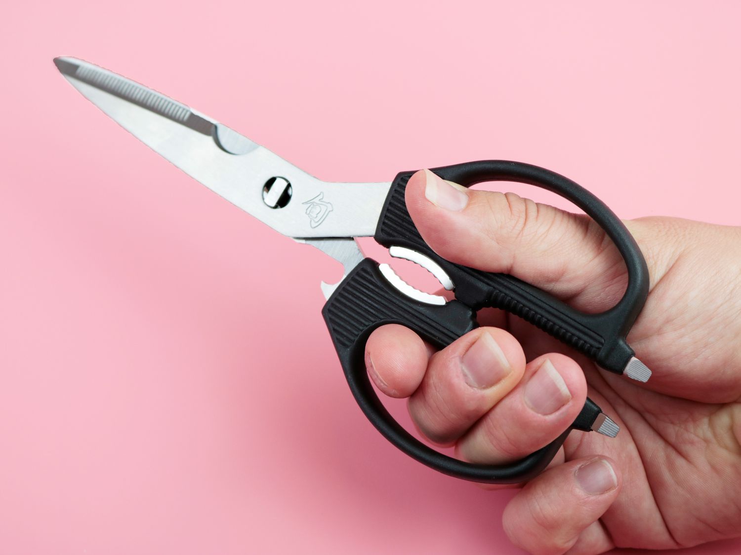 a hand holding kitchen shears and showing off bonus features on the handle