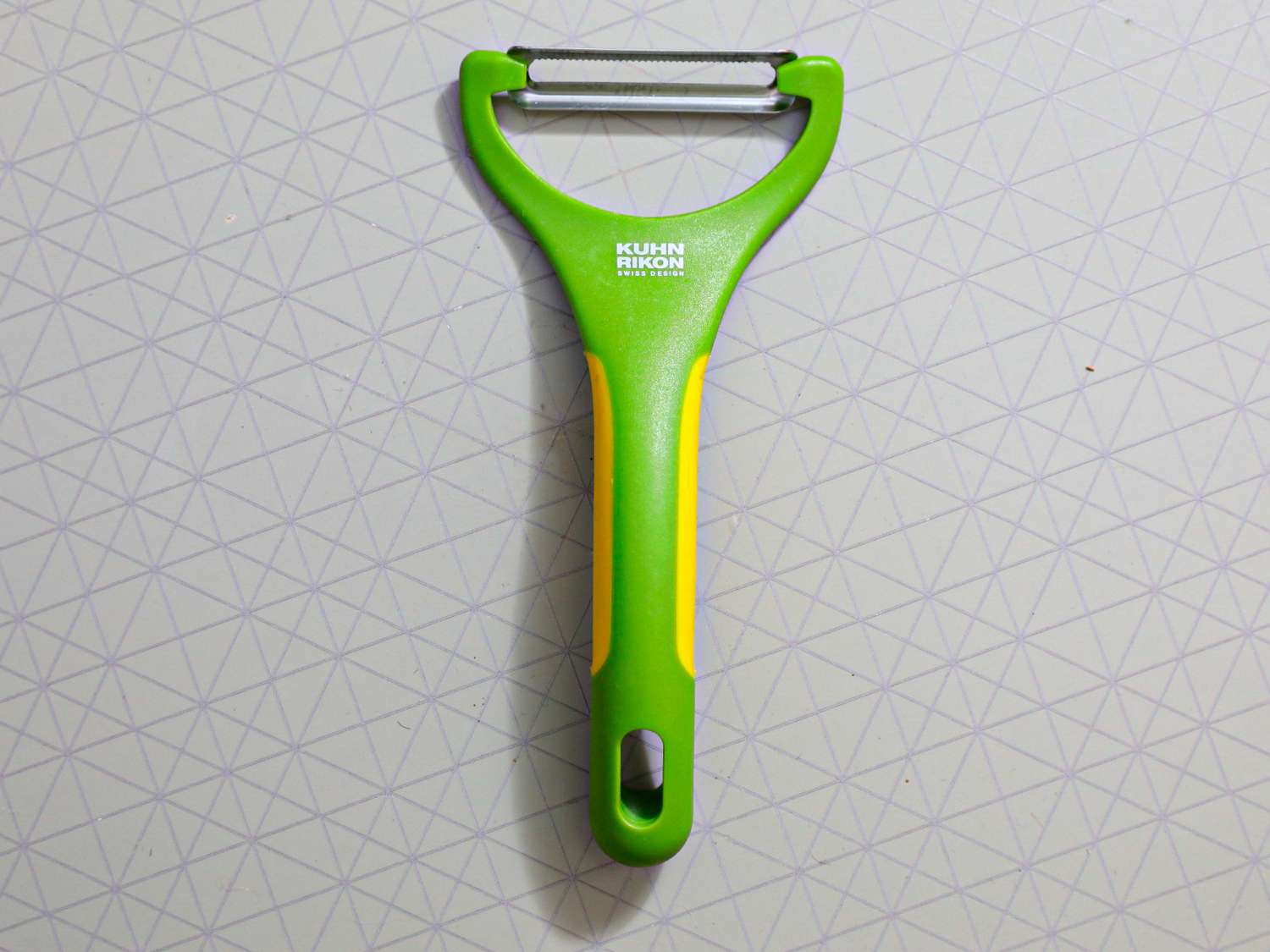 A green kuhn rikon peeler on a grey surface