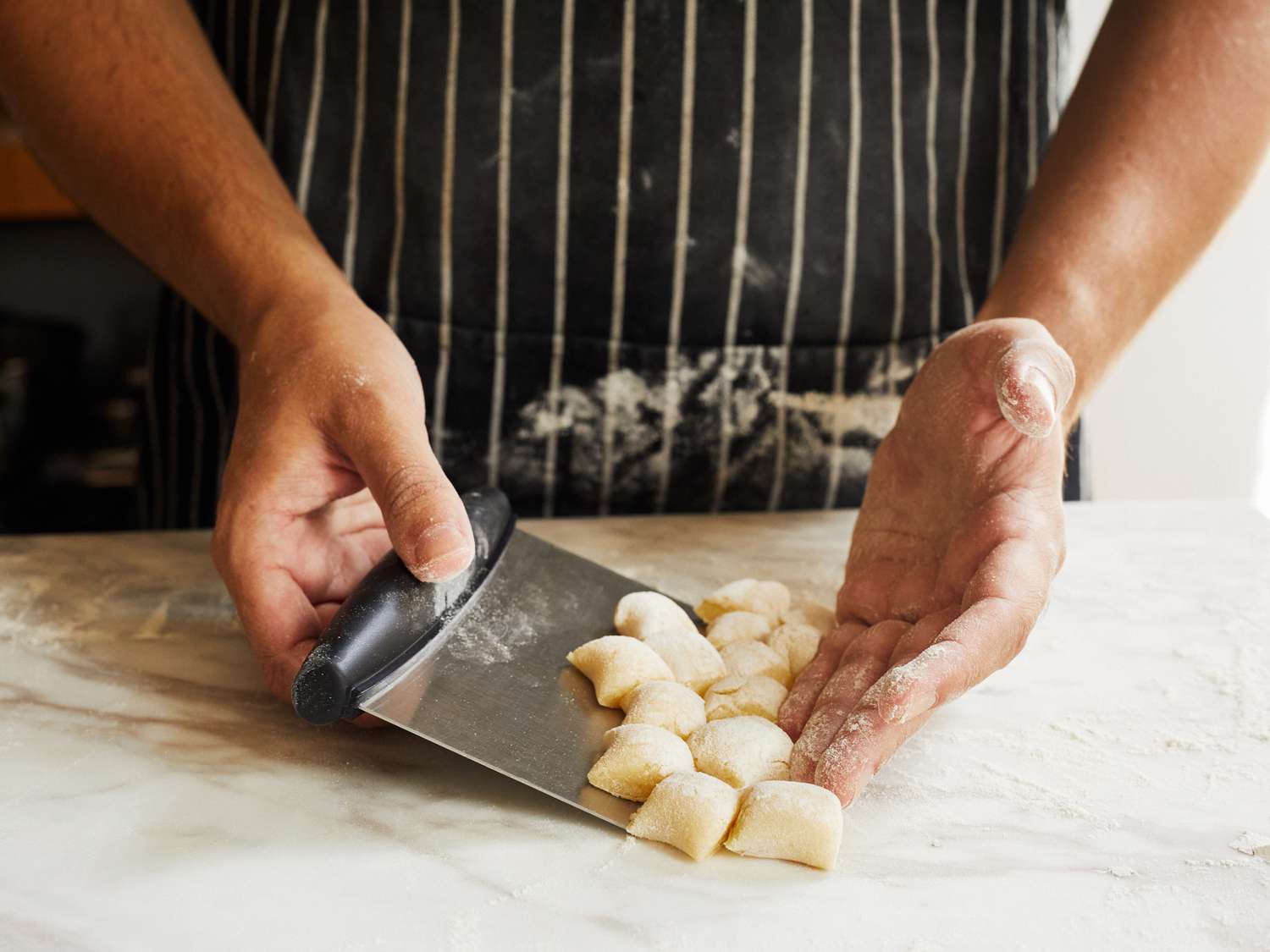 Using the OXO bench scraper to scrape up gnocchi dough on a floured marble countertop