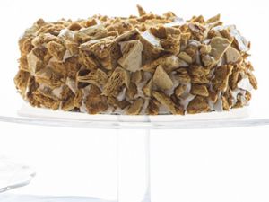 A loaf of Blum's Coffee Crunch Cake on a glass cake stand. The cake is covered with shards of honeycomb candy on all sides.