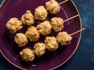 Three wood skewers with 4 squid balls each on a purple plate set against a blue background