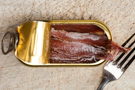 Overhead view of a tin of anchovies, partially opened to reveal the deboned fillets inside.