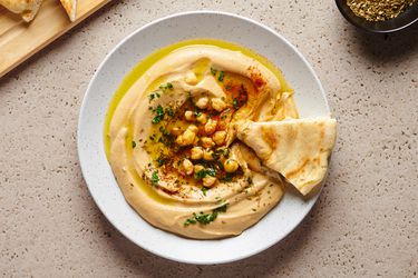 最好的我光滑的鹰嘴豆泥n a white round dish, with a piece of pita bread on the right hand side of the plate.