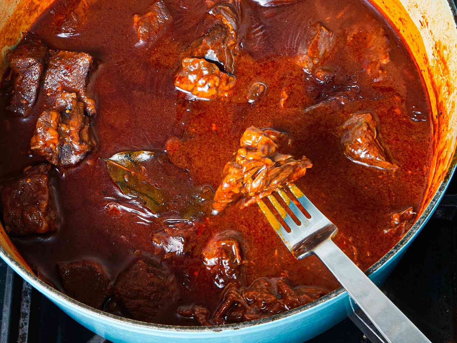 Fork lifting up a piece of tender meat from the pot