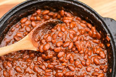 A crock of barbecue beans being stirred with a wooden spoon.