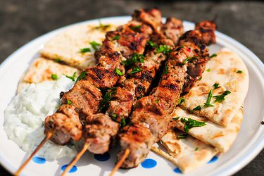 Three skewers of pork souvlaki on a plate with pita bread and tzatziki.