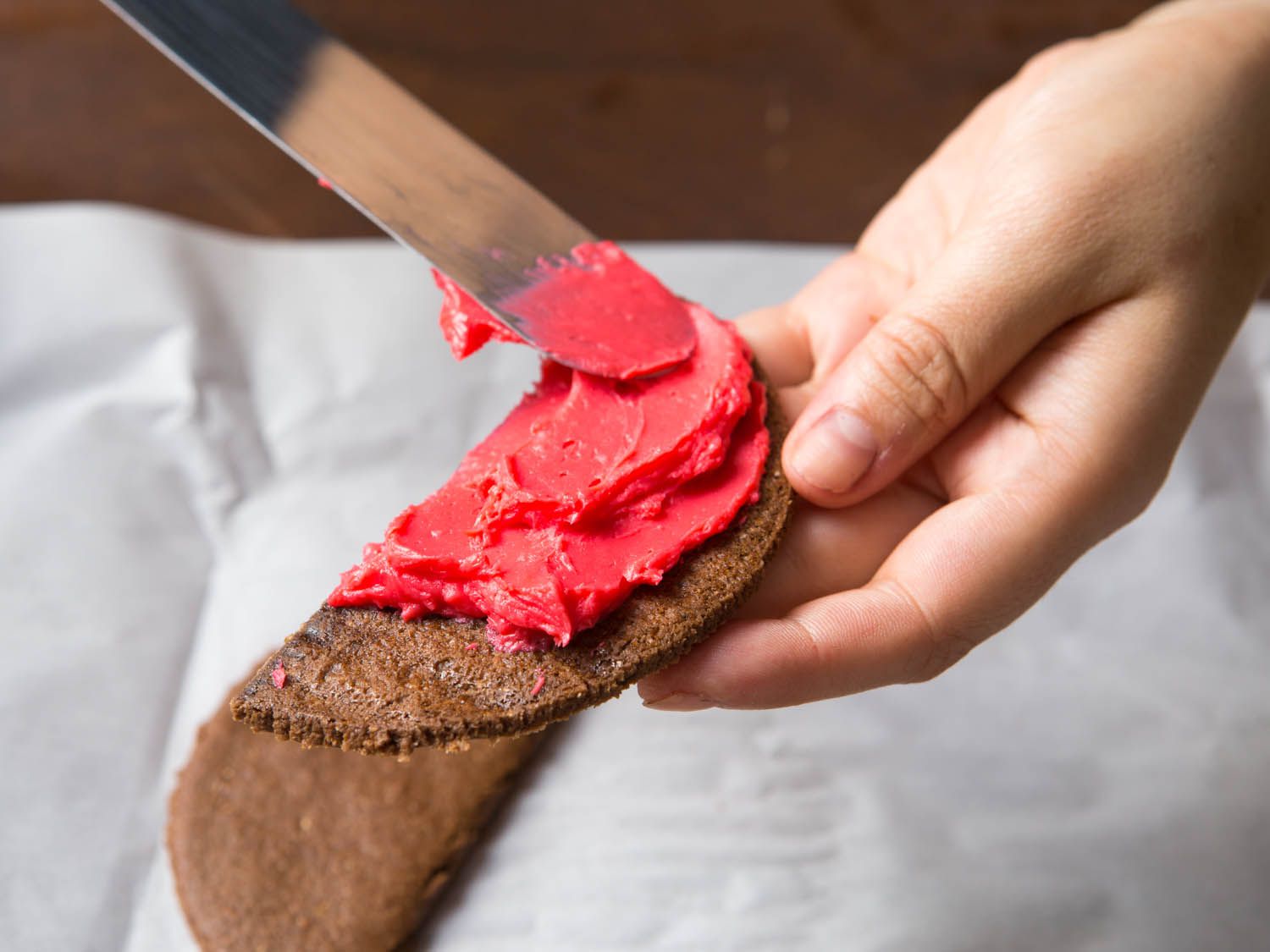 Spreading a tablespoon of red frosting onto a half disk of chocolate graham cracker.