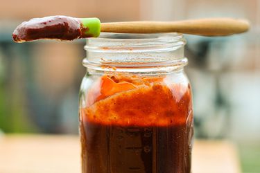 一个装满自制樱桃烧烤酱的石匠罐子，一个蘸着酱汁的硅胶糕点刷铺在罐子的边缘。