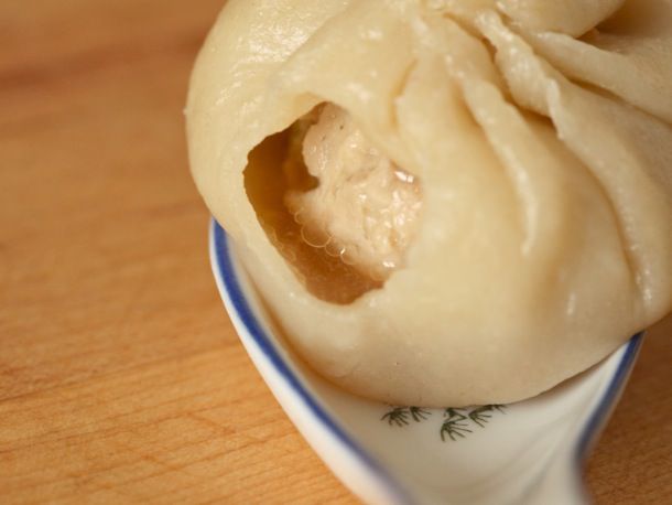 小龙包完饺子的特写soup spoon. A small bite has revealed the soupy interior and ball of filling swimming inside.