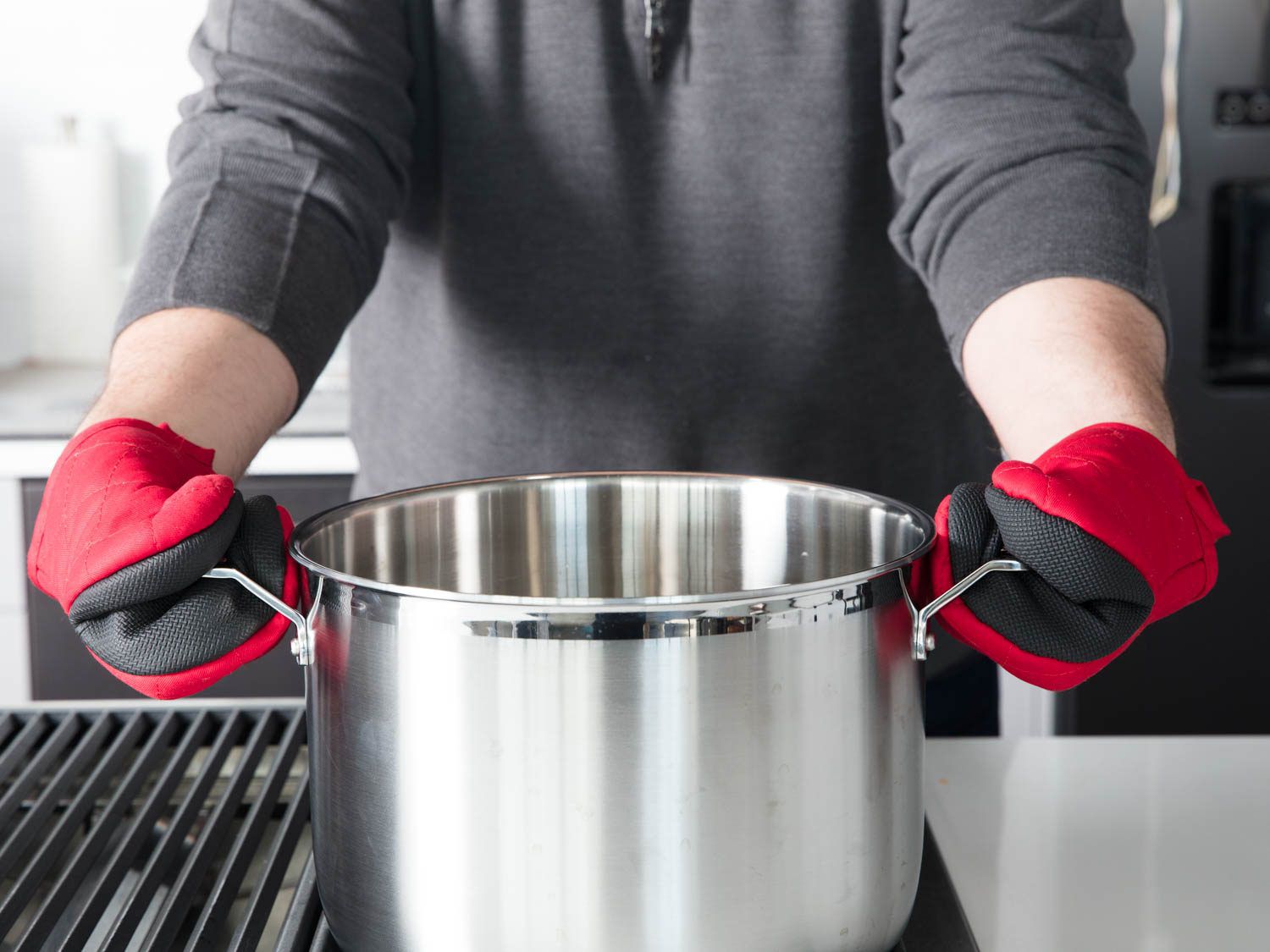 Two hands with oven mitts on gripping the handles of a stockpot