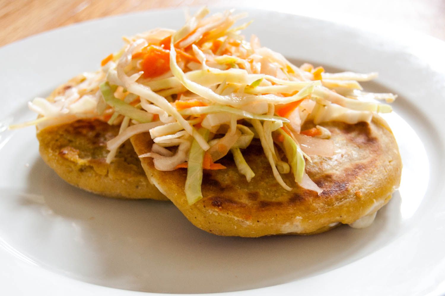 盘子里放着两份萨尔瓦多pupusas，上面放着一种叫做curtido的沙拉。