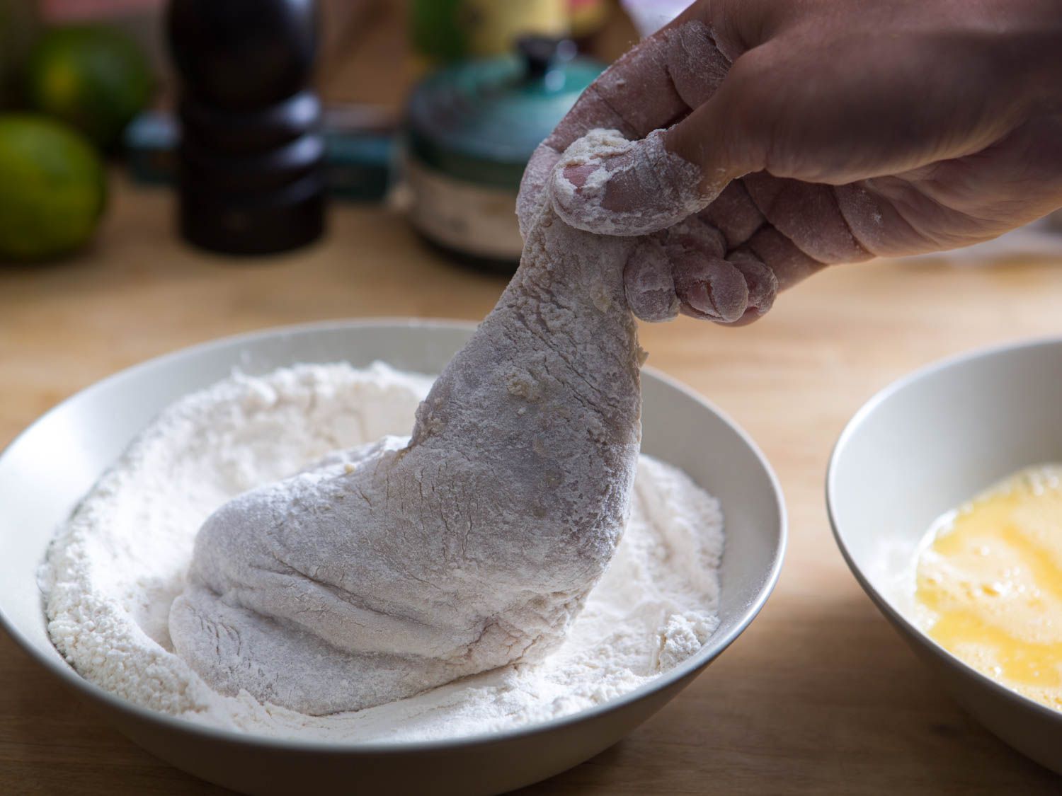 Dredging chicken leg in bowl of flour