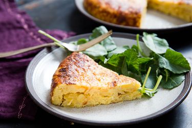 A slice of Spanish potato and onion tortilla on a small grey plate with salad on the side.