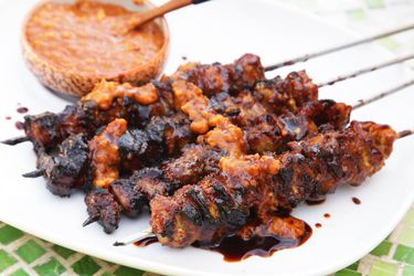 Chargrilled Balinese pork satays on a plate with peanut sauce