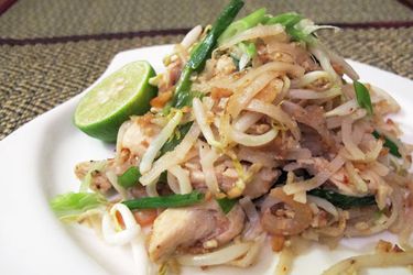 Side view of a plated chicken pad thai garnished with fresh lime.