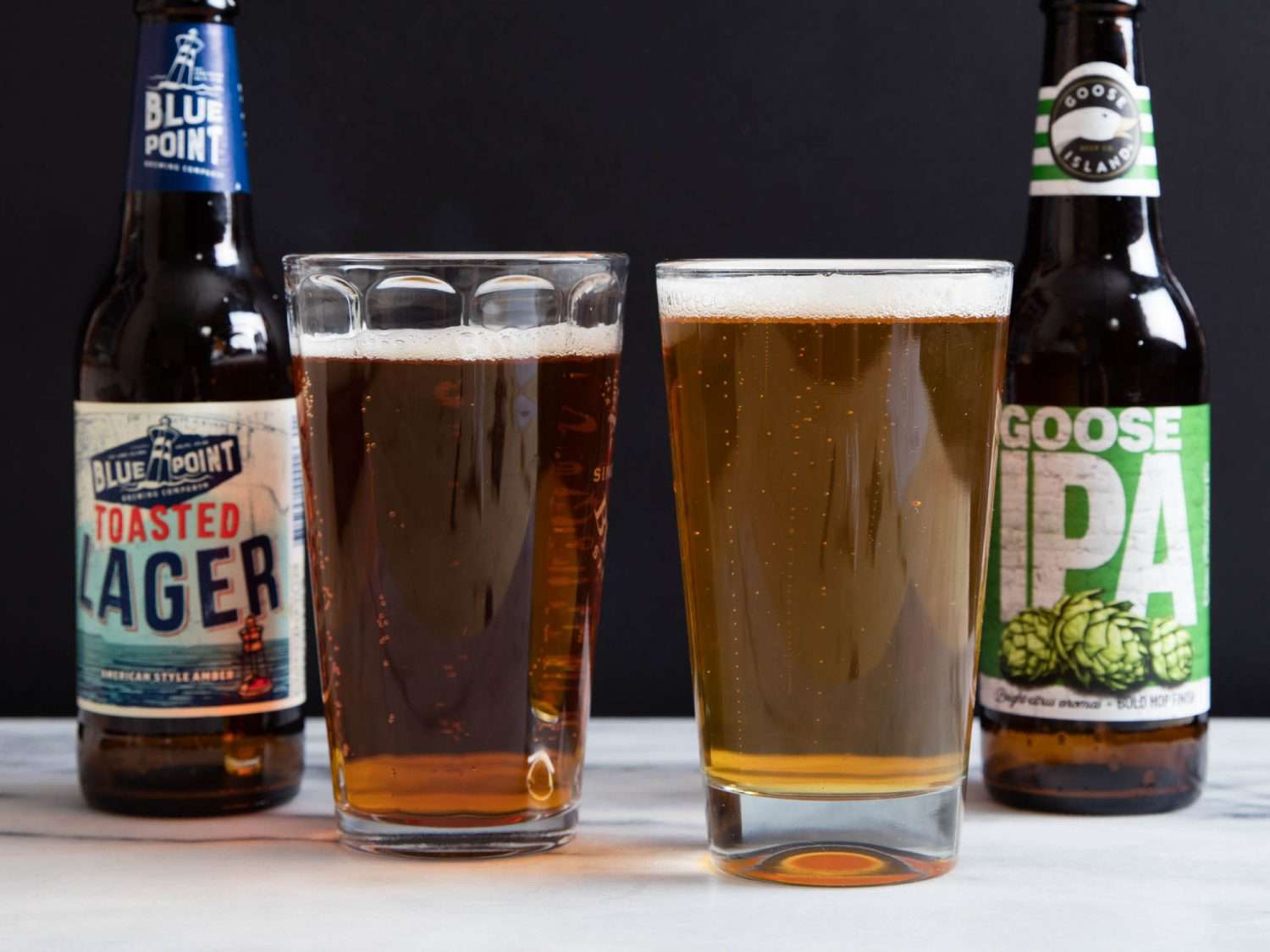 A lager and an IPA, each poured in glasses with the bottles next to the beer.