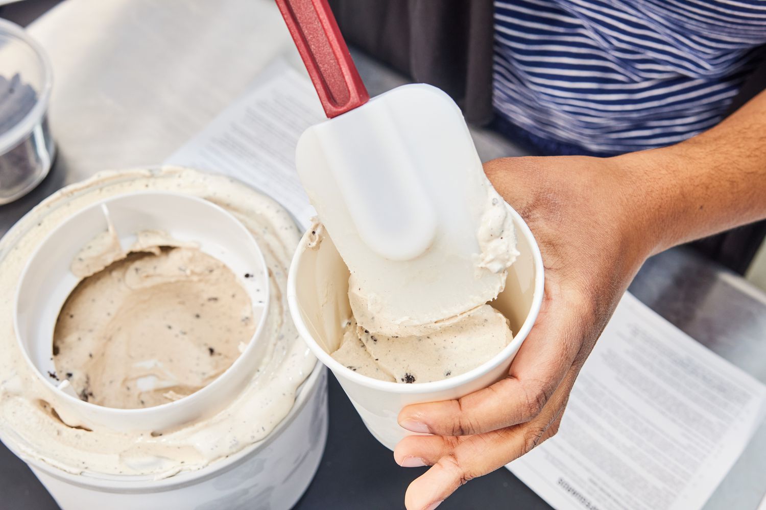a person using a spatula to move ice cream from an ice cream maker's bowl to a container